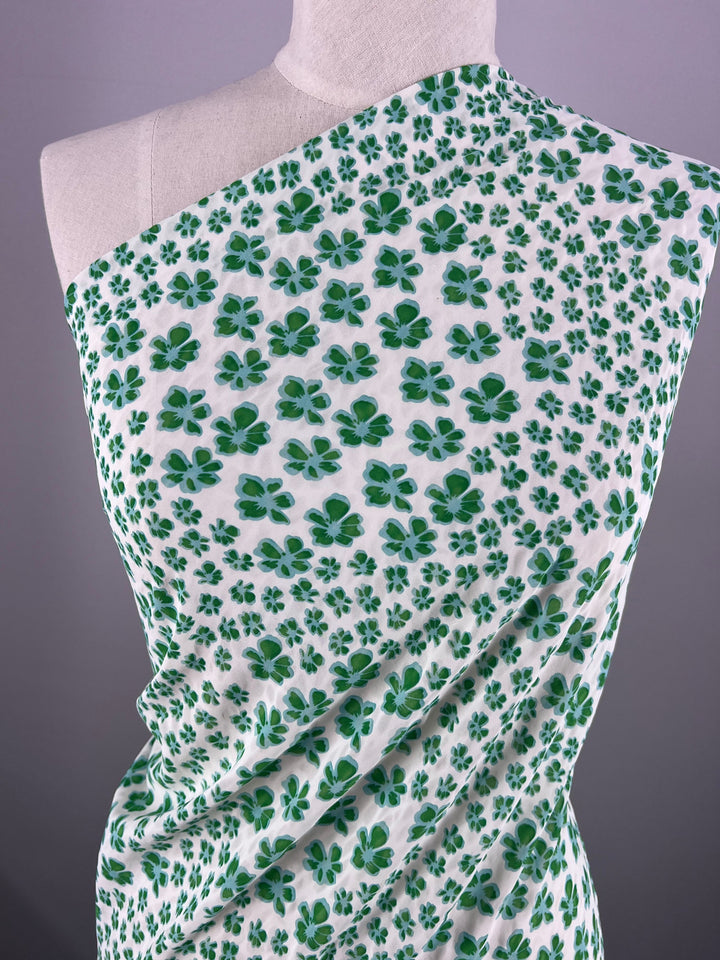 A mannequin displays elegant "Salt Shrunk Print - Smurf - 155cm" fabric by Super Cheap Fabrics, featuring a green clover leaf pattern on a white background against a gray backdrop.