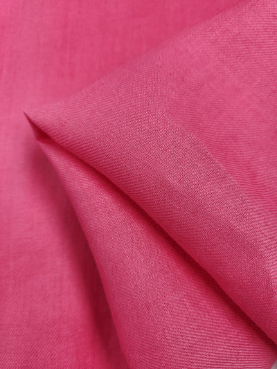 A close-up of the folded Pure Washed Linen in hot pink from Super Cheap Fabrics showcases its smooth texture and visible weave pattern. The lightweight fabric is neatly creased, highlighting its vibrant color and exquisite material details across its 140cm width.