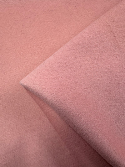 A close-up of soft, coral almond Wool Cashmere fabric from Super Cheap Fabrics shows its smooth texture. Folded lines create gentle shadows, while the muted blush color enhances its luxurious softness, offering a warm impression perfect for year-round use. Fabric width: 150cm.
