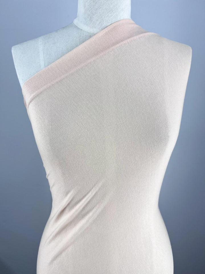 A mannequin displays Super Cheap Fabrics' Summer Cotton Knit in Cream Tan, a form-fitting, one-shoulder dress with perfect stretch, against a plain gray backdrop.