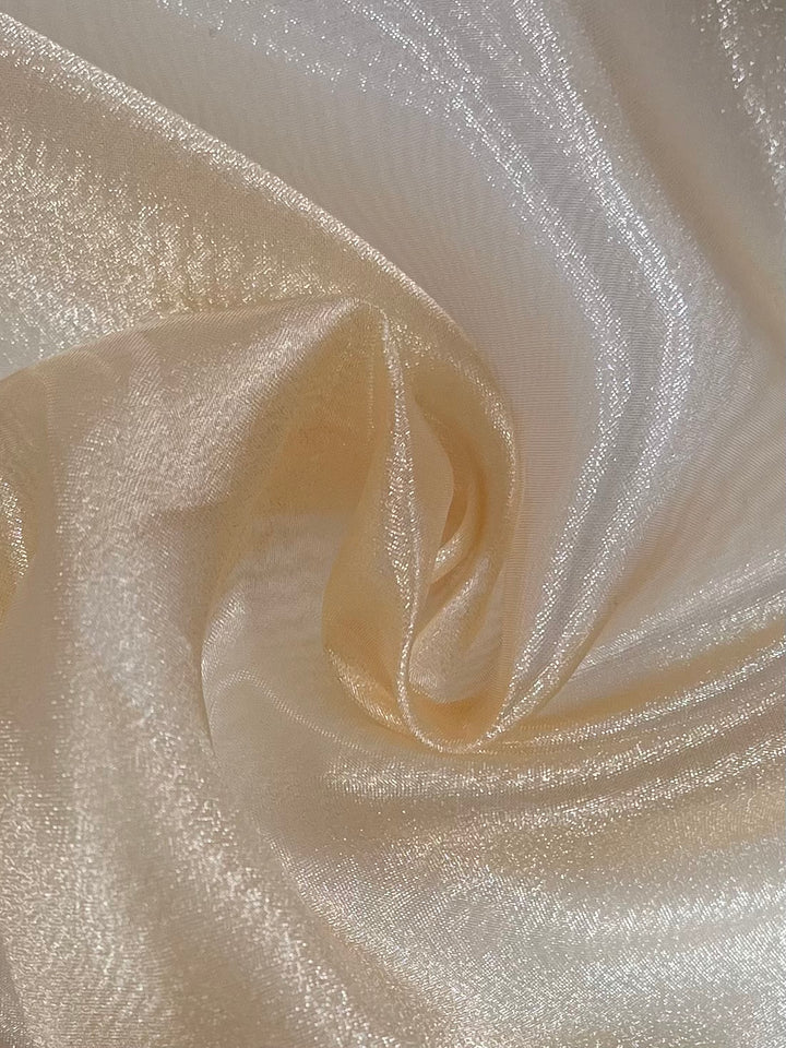 A close-up of Super Cheap Fabrics' Organza - Sundress - 150cm fabric reveals intricately folded shimmering ivory organza, creating soft, flowing waves. The smooth, glossy texture subtly reflects light for a luxurious and elegant appearance.