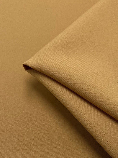 A close-up of Panama Suiting - Mustard- 150cm from Super Cheap Fabrics with a smooth texture. The medium weight fabric is folded diagonally, showcasing the fine weave and soft appearance. The lighting emphasizes the even color and surface quality of the material.