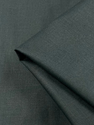 A close-up view of Superfine Suiting in Darkest Spruce from Super Cheap Fabrics showcases its texture. The fabric is neatly folded with a visible crease, and the smooth, slightly reflective surface indicates a fine polyester weave.