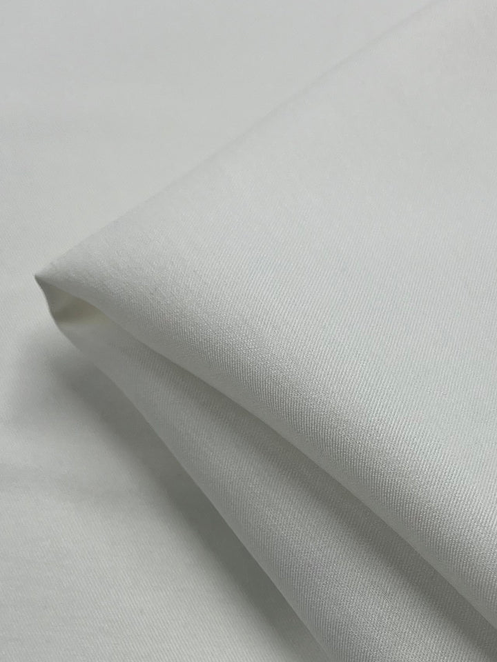 A close-up of a neatly folded piece of the Mercerised Cotton - Ivory - 148cm from Super Cheap Fabrics shows its lightweight fabric with a smooth texture. The edges are visible against a plain white background, accentuating its fine weave and pristine appearance.