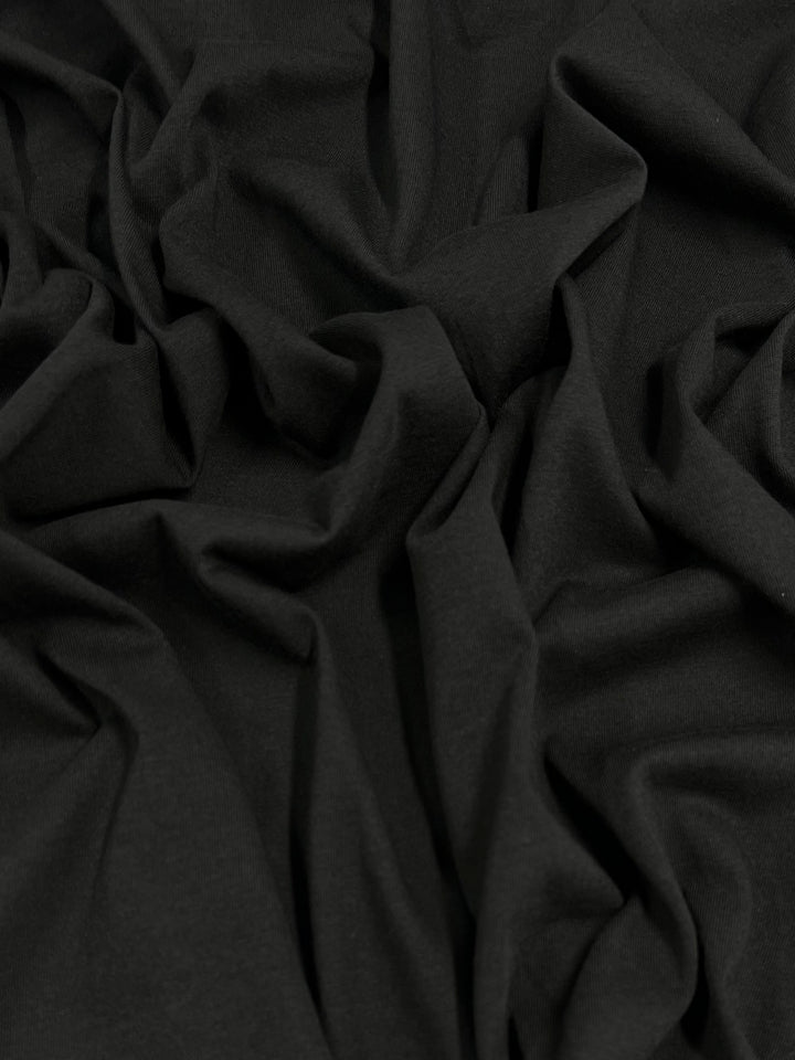 The Cotton Jersey - Black by Super Cheap Fabrics measures 142cm wide and is crafted from 100% cotton. This lightweight fabric has a crinkled, soft texture with subtle folds, perfect for combining comfort and style.