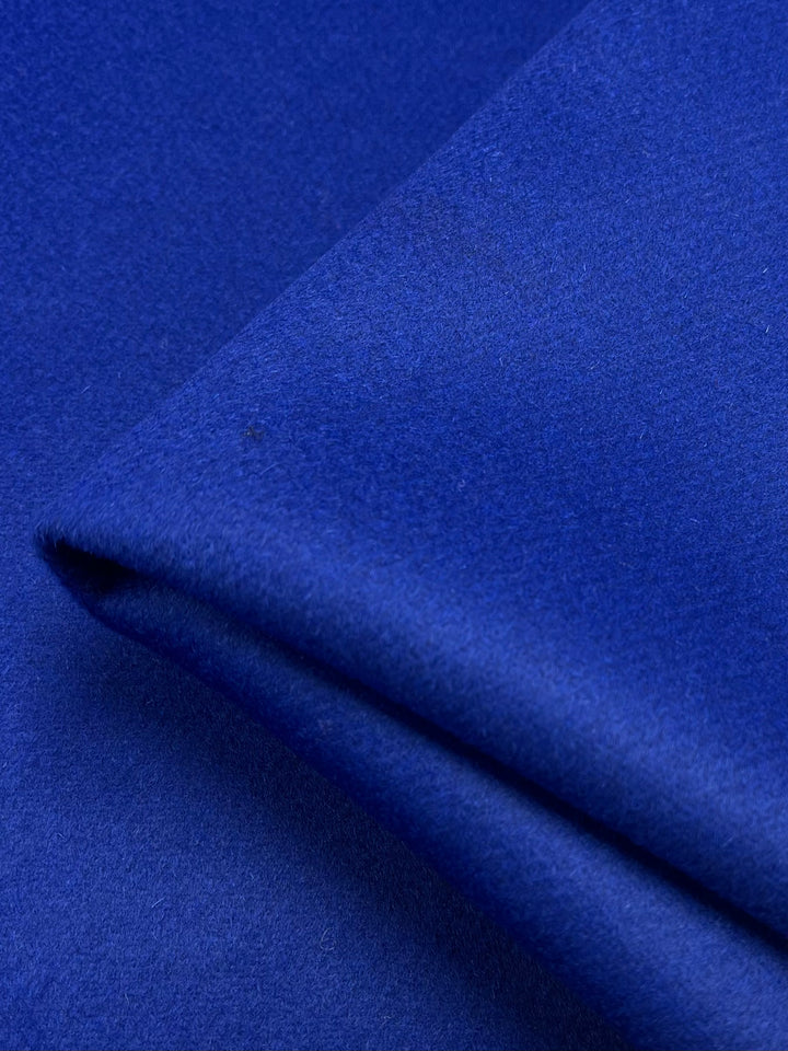 A close-up of a smooth, royal blue fabric with a folded edge, highlighting its rich color and soft texture. The heavy weight Wool Cashmere - Cobalt - 150cm by Super Cheap Fabrics appears dense and luxurious to touch.