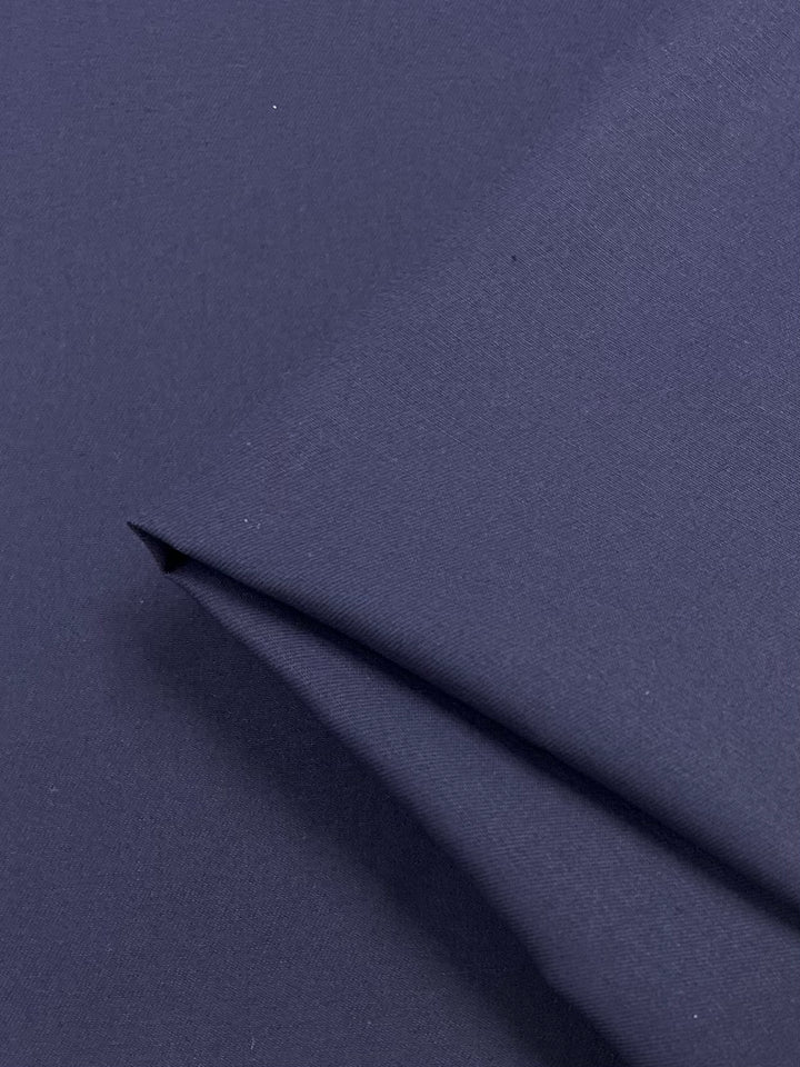 The Super Cheap Fabrics Cotton Drill in Navy, 150cm, features a close-up of the slightly folded fabric, highlighting its smooth and even texture—ideal for crafting durable workwear trousers.