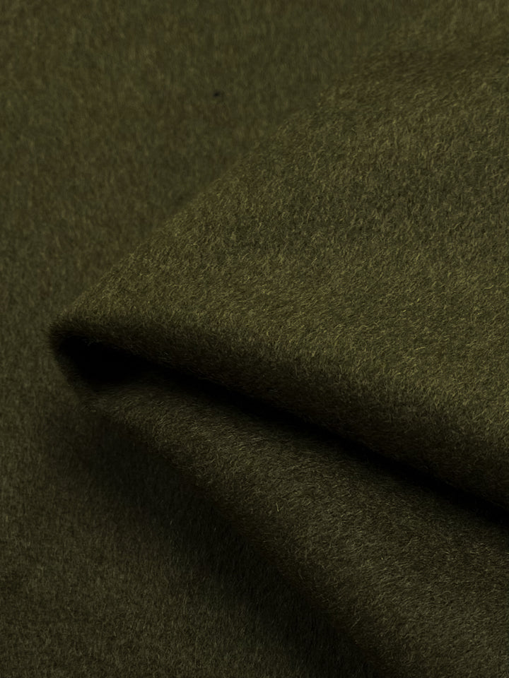 A close-up of a folded piece of extra heavy weight Wool Cashmere fabric in a rich Green Olive color from Super Cheap Fabrics, showcasing its soft and slightly fuzzy texture. The material appears thick and warm, making it ideal for clothing or furnishings. Dry clean only.