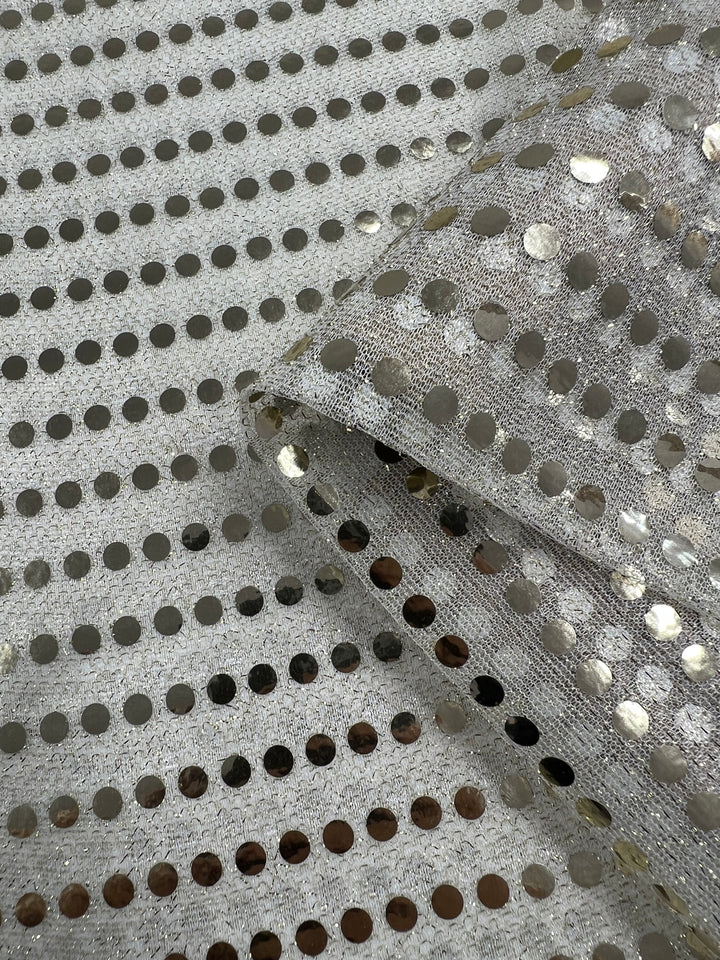 Close-up of the Sequin - White Gold - 112cm fabric from Super Cheap Fabrics, featuring a shiny black appearance with a silver base and metallic circular sequins evenly spaced throughout. The dancewear fabric is slightly folded, creating an eye-catching shine as light reflects off the sequins.