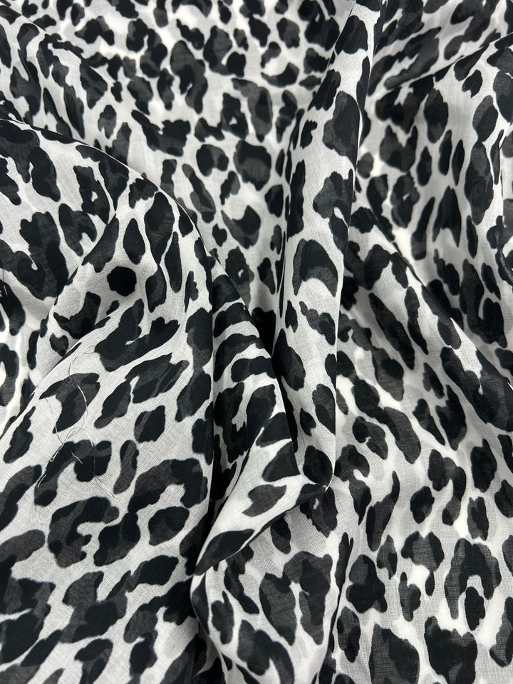 The Pure Printed Silk Voile - Snow Leopard - 145cm from Super Cheap Fabrics is an extra lightweight fabric that features a striking black and white leopard print design. The silk cotton material is soft and drapes beautifully, with visible folds and creases that accentuate its pattern and texture—ideal for creating stunning dresses.