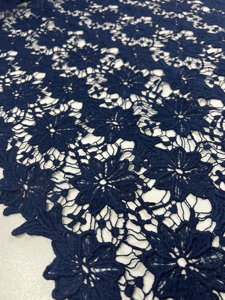 Close-up of Anglaise Lace - Bloom - 120cm in dark blue from Super Cheap Fabrics, showcasing its intricate floral patterns, perfect for bridal wear. This lace features a repeating design of flowers linked by fine, thin threads, creating a delicate and elegant texture against a blurred white background.