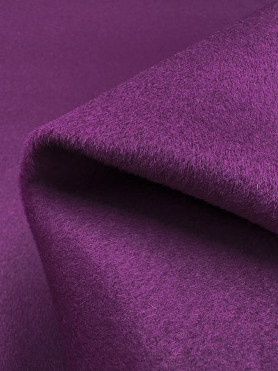 Close-up image of a folded piece of soft, textured fabric in a deep magenta shade. The Super Cheap Fabrics Wool Cashmere - Magenta - 150cm material has a slightly fuzzy appearance, highlighting its plush and cozy nature.