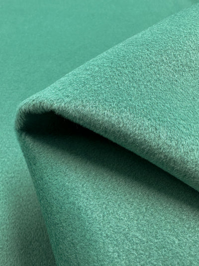 Close-up image of a folded, soft green fabric with a slightly textured surface, displaying its plush and smooth texture. The heavy weight fabric appears to be fleecy and thick, suggesting warmth and comfort. This is the Wool Cashmere - Agate Green - 150cm from Super Cheap Fabrics.