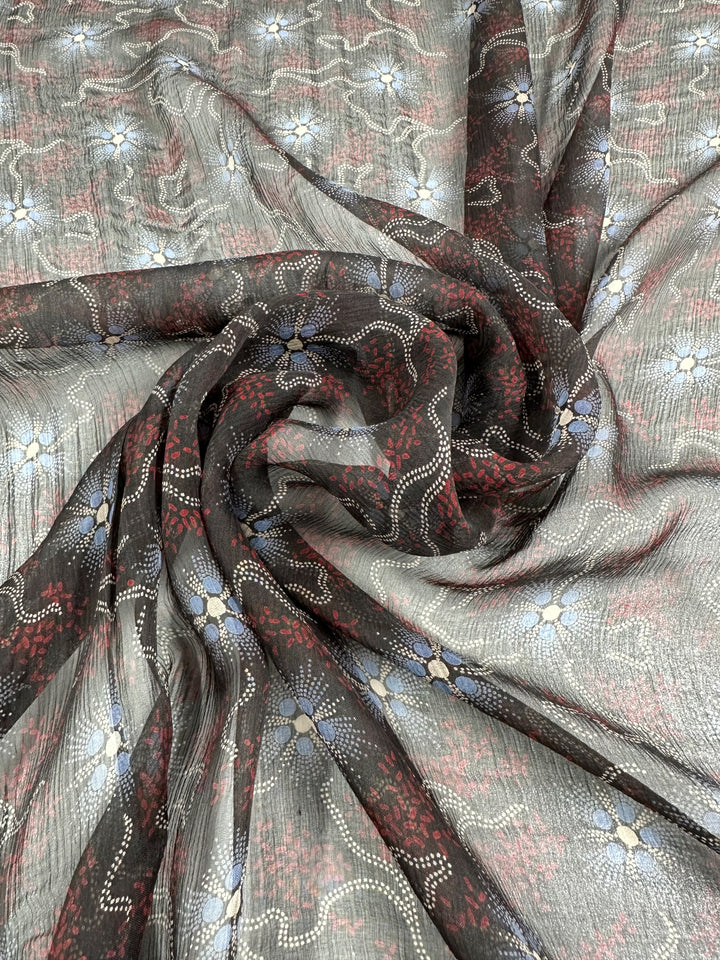 The Pure Printed Silk - Artisan - 140cm from Super Cheap Fabrics features delicate floral patterns with intricate white and red dotted lines on a dark background. The fabric is artfully arranged in gentle folds, highlighting its texture and design, making it perfect for high-end fashion projects.