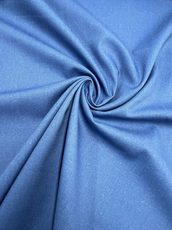 Close-up of the Linen Blend - Denim from Super Cheap Fabrics, artfully arranged in a spiral fold pattern. This textile, with its vibrant blue hue reminiscent of fine upholstery, showcases a smooth texture and creates a dynamic sense of movement.