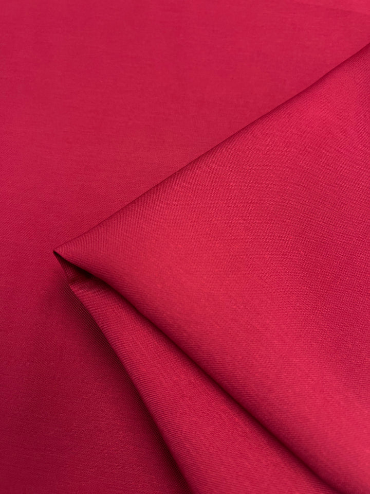 A close-up of the rich Barkeycorn Red twill from Super Cheap Fabrics showcases its smooth texture. This medium-weight suiting fabric, 145cm wide, is neatly folded, highlighting sharp lines and shadows that enhance its vibrant diagonal weave.