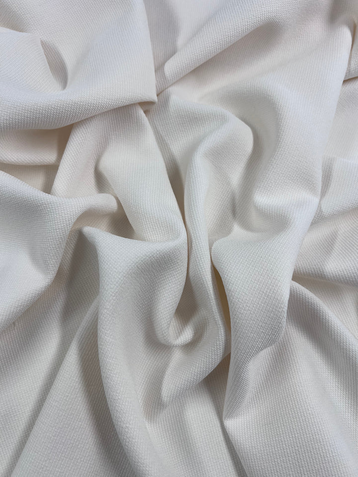 A close-up of hopsack suiting in ivory from Super Cheap Fabrics, 135cm wide, reveals its versatile waffle-like texture. The material drapes unevenly, forming soft folds and shadows similar to twill suiting.