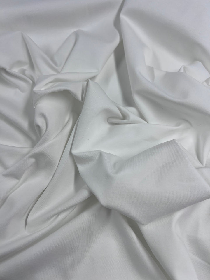 A close-up of crumpled medium-heavy fabric showcases folds in varying ivory shades, highlighting the soft texture typical of Super Cheap Fabrics' Cotton Lycra - Ivory - 170cm.