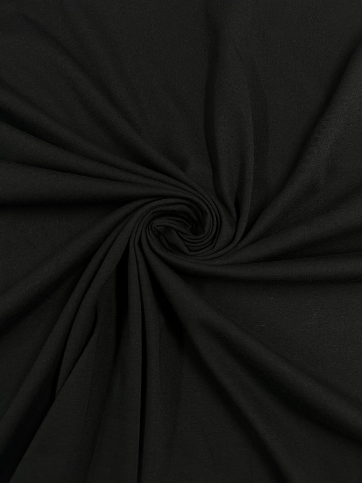 A close-up of the Super Cheap Fabrics' Cotton Jersey - Black - 142cm shows the 100% cotton fabric twisted into a spiral. Its folds radiate outward, creating a dynamic look with a smooth, slightly glossy texture.