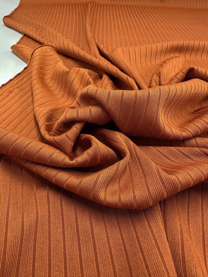 The medium-weight Rib Knit - Rust by Super Cheap Fabrics features prominent vertical ribbing in a warm burnt-orange shade with soft, slightly glossy texture and generous stretch, draping beautifully at 175cm wide.