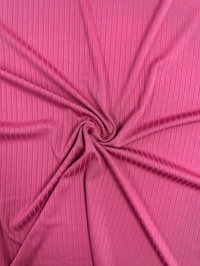 A close-up of Super Cheap Fabrics' Rib Knit in Lilac Rose (170cm) shows the medium weight fabric's swirl pattern with vertical lines. The pink fabric has a soft, flowing texture that emphasizes its stretch and comfort.