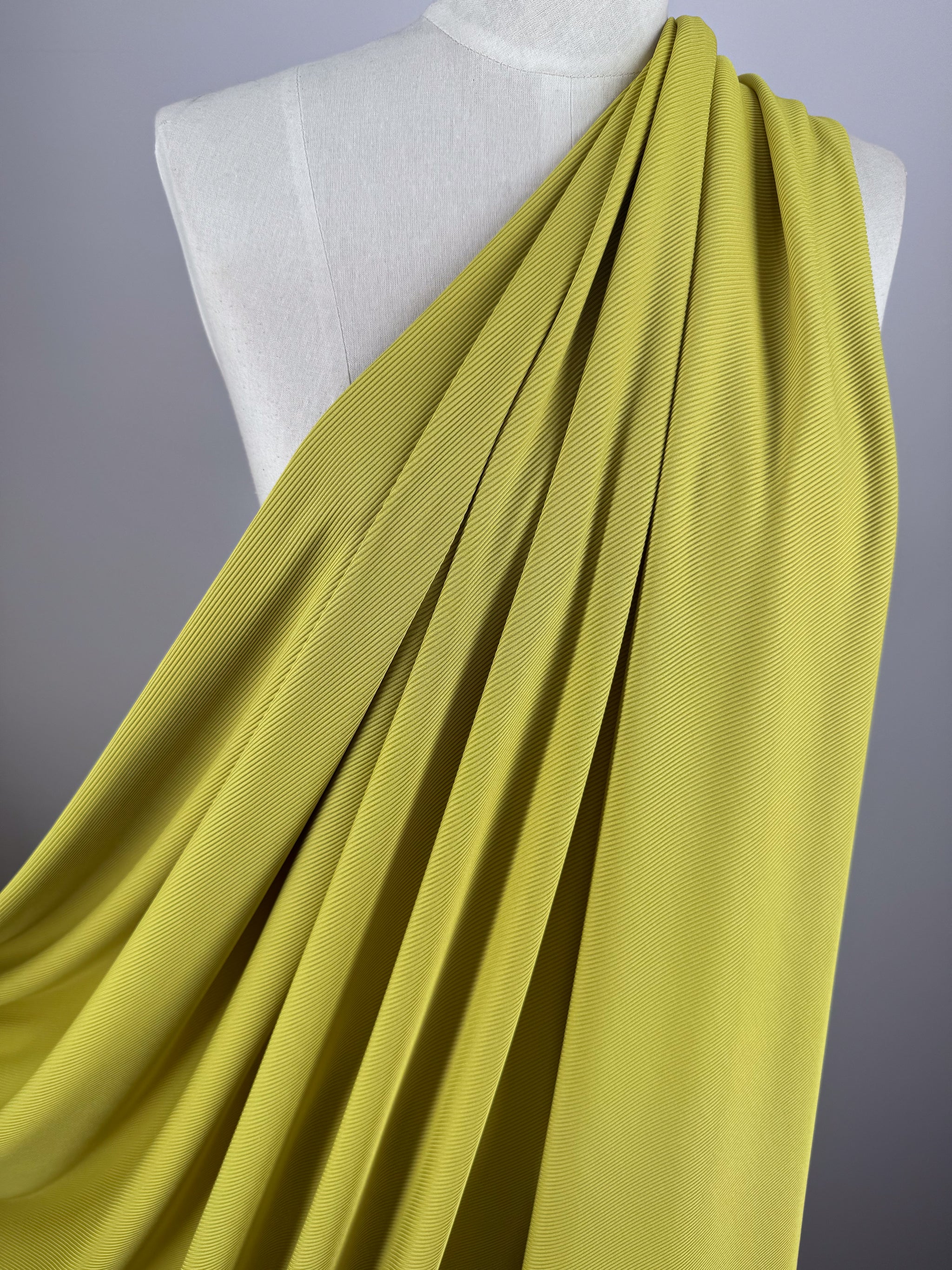 The Rib Knit 1x1 - Squash by Super Cheap Fabrics flows elegantly over a white mannequin torso, highlighting its smooth texture and folds against a plain gray background.