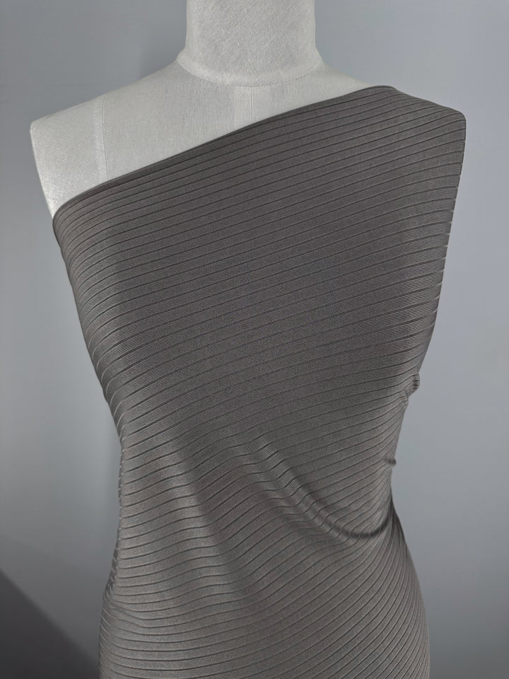 A mannequin showcases Super Cheap Fabrics' Rib Knit in Dark Grey (170cm), wrapped asymmetrically over one shoulder against a neutral background, emphasizing the fabric's texture and folds.