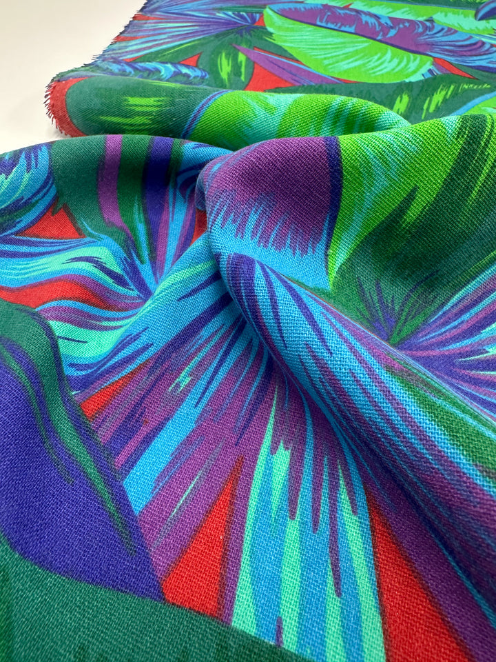 The "Cotton Duck - Palm Lush Meadow - 140cm" by Super Cheap Fabrics is a vibrant, medium-weight cotton featuring bold, abstract tropical designs in blue, green, and purple. Its soft feel and slightly gathered texture make it perfect for adding color to home décor projects.