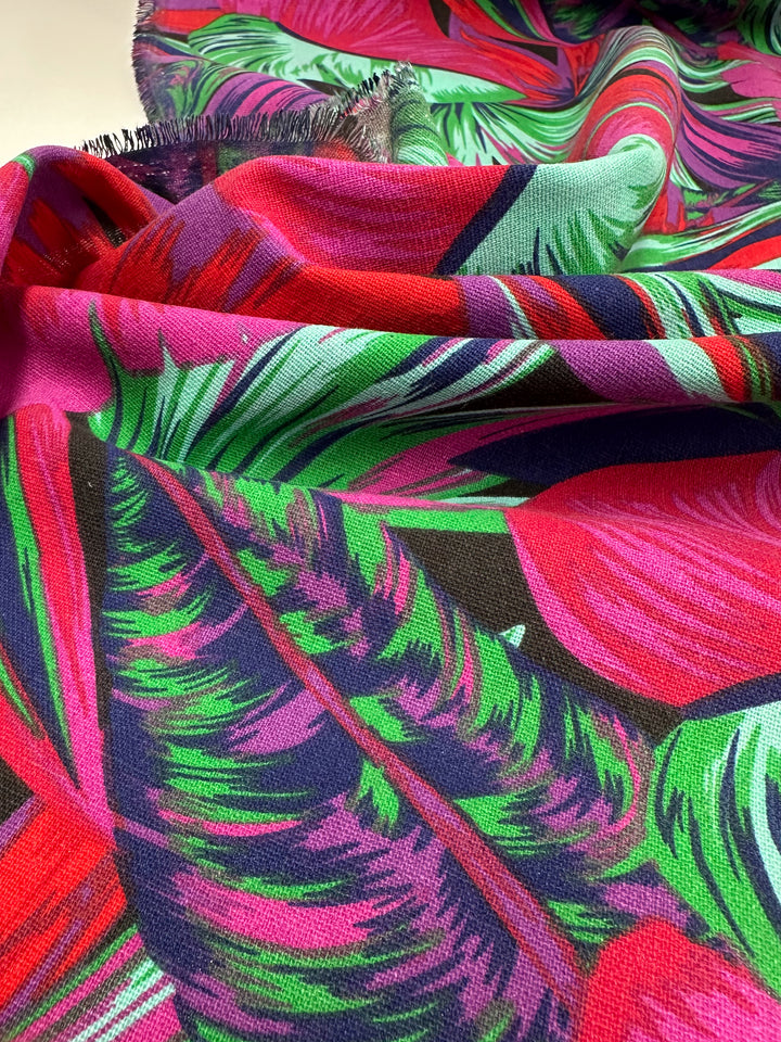 Close-up of the vibrant Cotton Duck "Palm Cockatoo" fabric by Super Cheap Fabrics, featuring a colorful tropical leaf design in pink, green, red, and purple. This 140cm medium-weight cotton is draped and slightly textured, ideal for bold home décor projects.