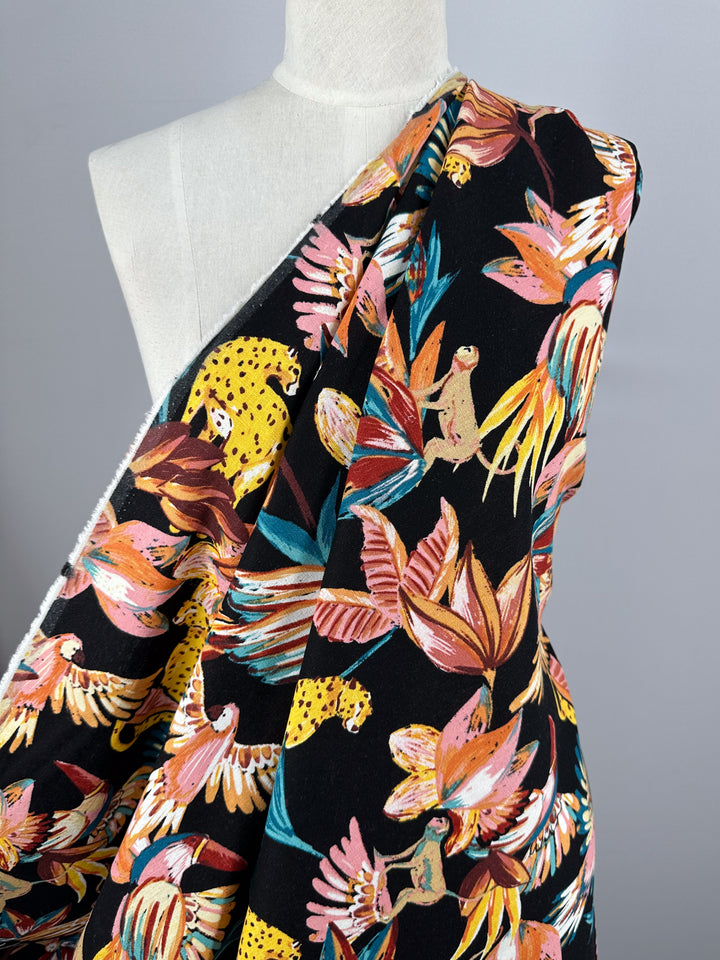 A mannequin displays Super Cheap Fabrics' Linen Blend - Paradiso Black, featuring a tropical print with sloths, leopards, and parrots among colorful leaves on a black background.