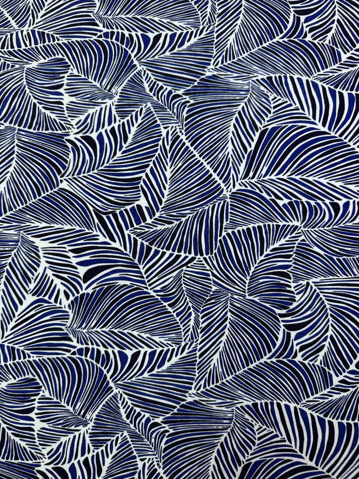 The Printed Lycra - Sapphire fabric by Super Cheap Fabrics features an abstract, symmetrical design of overlapping navy blue and white leaf-like shapes. Its striped texture adds vibrancy and complexity, perfect for garments. Made from Polyester/Spandex, it measures 150cm in width.
