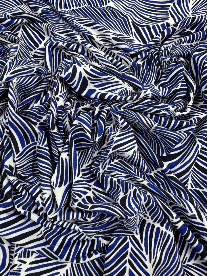 Close-up of Super Cheap Fabrics' Printed Lycra - Sapphire, 150cm wide, with a crumpled look. Featuring bold abstract dark blue stripes and shapes on a white background, its Polyester/Spandex blend offers a textured, soft appearance resembling natural motifs.