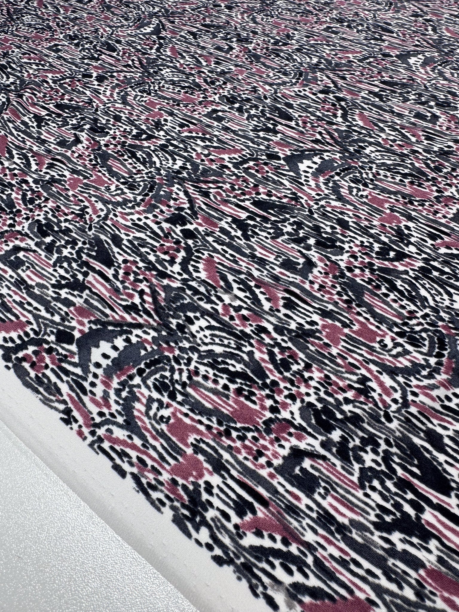 A close-up of Super Cheap Fabrics' Printed Lycra in Grey Musk highlights a medium-weight Polyester/Spandex blend with an abstract black, pink, and white pattern featuring dots, lines, and organic shapes for a dynamic texture. Product width: 150cm.
