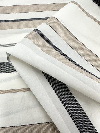 Close-up of Super Cheap Fabrics' Cotton Voile - Creamy Nimbus - 155cm, showcasing its horizontal stripes in shades of black, brown, and beige. The lightweight fabric is folded over itself, revealing its breathable texture and pattern.