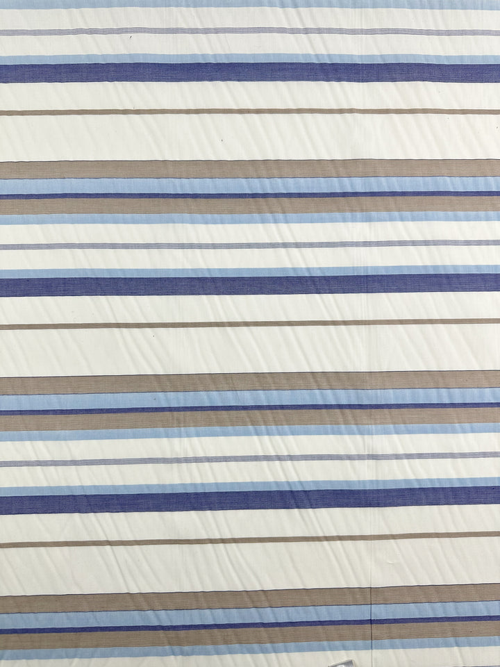 Introducing the "Blue Breeze" Cotton Voile from Super Cheap Fabrics, featuring horizontal stripes in alternating shades of blue, gray, and white. This 100% cotton fabric has stripes of varying widths that are evenly spaced to create a harmonious pattern across its 155cm width. Perfectly suited for crafting light and airy garments.