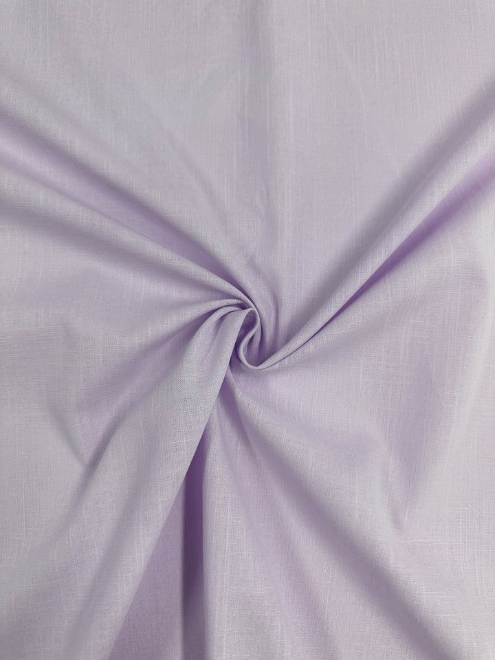 A close-up of Super Cheap Fabrics' Linen Blend - Orchid Hush - 145cm reveals a soft, smooth texture. The lightweight linen fabric is skillfully gathered and twisted at the center, forming gentle folds and shadows that radiate outwards from the twist. Made in Italy, the material showcases a subtle crisscross pattern on its surface.