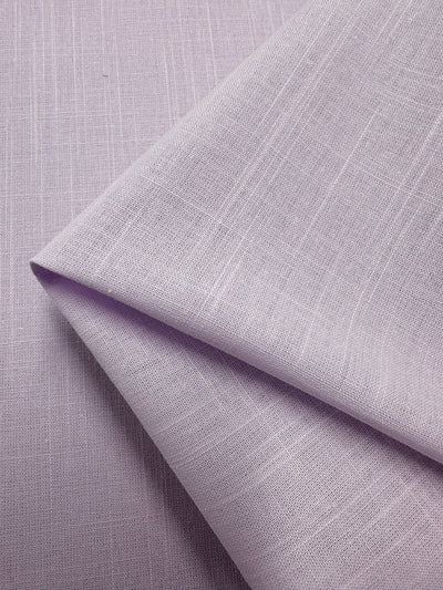 A close-up of lilac-colored linen blend fabric with a subtle texture. The lightweight fabric, neatly folded at one corner, showcases its smooth surface and fine weave. This exquisite piece from Super Cheap Fabrics is named Linen Blend - Orchid Hush - 145cm and is made in Italy.