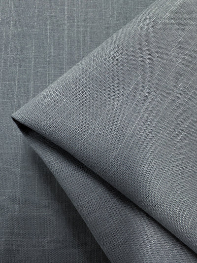 Close-up of the Ghost Gray Italian linen blend fabric by Super Cheap Fabrics, folded at a diagonal. This 145cm lightweight fabric features a slightly rough texture with a visible weave pattern, showcasing fine, precise lines and a matte finish.