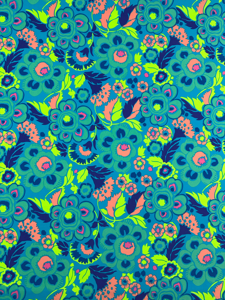 The Printed Nylon Lycra - Mirage - 158cm from Super Cheap Fabrics features a vibrant floral pattern, showcasing turquoise, green, pink, and dark blue flowers and leaves in a repetitive design on a teal background. This high-quality print is perfect for swimwear and features flowers that vary in size and style, creating a lively and intricate texture on light to medium weight fabric.