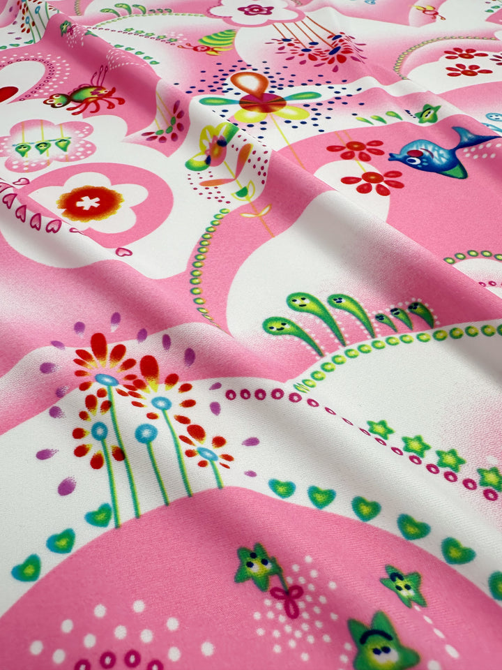 A detailed look at the vibrant and playful patterns of "Printed Nylon Lycra - Anime - 158cm" by Super Cheap Fabrics, perfect for swimwear. This high-quality fabric showcases an engaging mix of floral and abstract prints, featuring various flowers, dots, and whimsical shapes in bright pinks, greens, yellows, blues, and reds set against a contrasting white and pink background. The soft texture enhances the stunning quality of the print.