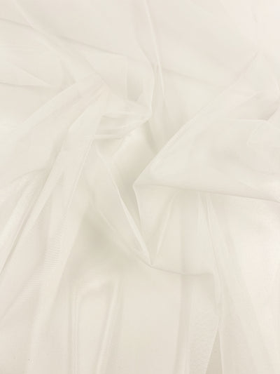 A close-up image of a piece of Soft Tulle - Ivory - 160cm by Super Cheap Fabrics with delicate folds and textures. The extra lightweight material is slightly transparent and has a soft, flowing appearance, perfect for dresses, creating gentle waves and light creases on the surface.