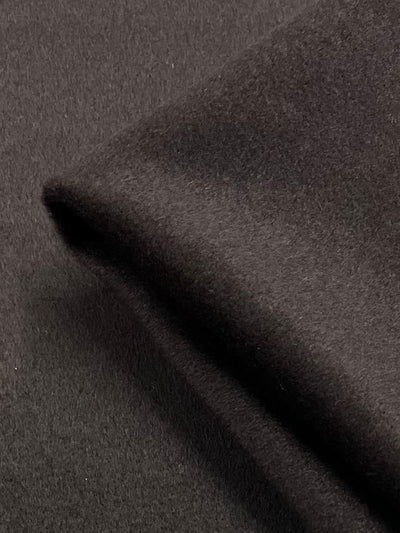 A close-up of folded black Wool Cashmere - Demitasse - 150cm from Super Cheap Fabrics with a smooth texture. The image shows the heavy weight fabric layered, highlighting its thickness and soft surface.