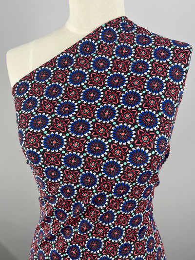 A mannequin dressed in a form-fitting, one-shoulder garment featuring Super Cheap Fabrics' Printed Nylon Lycra - Madalah - 150cm with vibrant geometric patterns and circular designs in shades of red, blue, and white against a black background. The swimwear fabric drapes elegantly across the body.