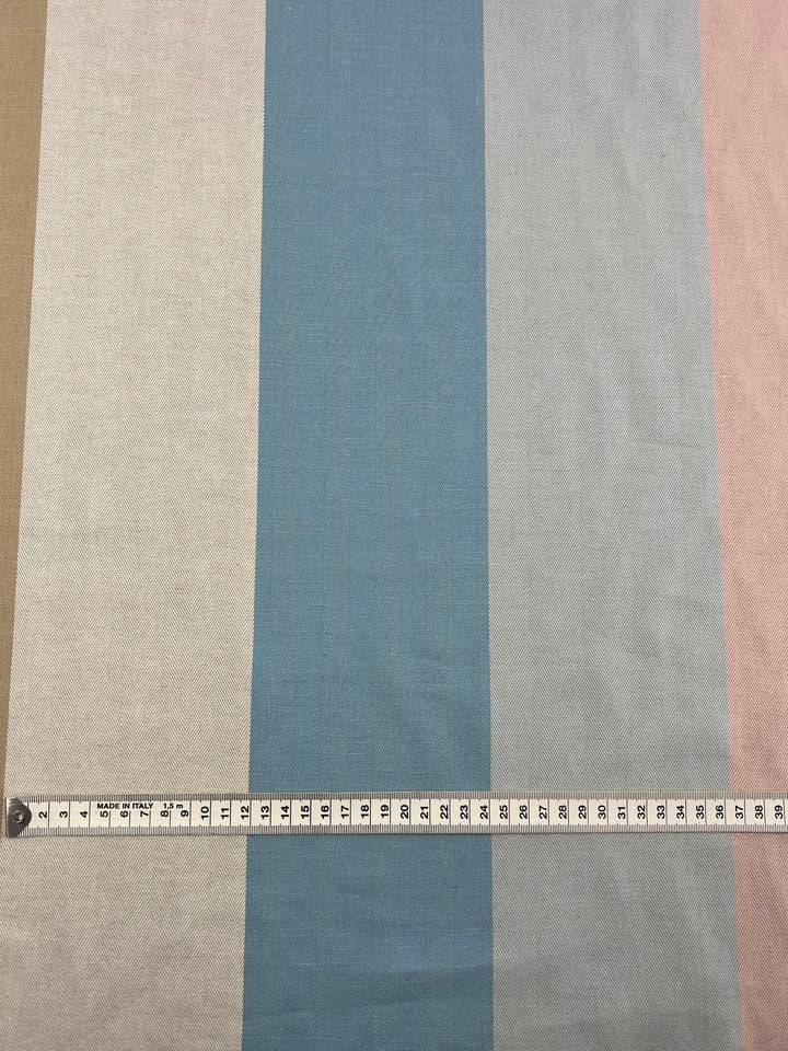 A fabric with vertical stripes in beige, white, blue, light blue, and pink is laid flat. A measuring tape, extended and slightly curved, stretches horizontally across the Designer Cotton - Blipe - 155cm from Super Cheap Fabrics and measures 20 inches. Crafted from sustainable deadstock materials for eco-friendly fashion lovers.