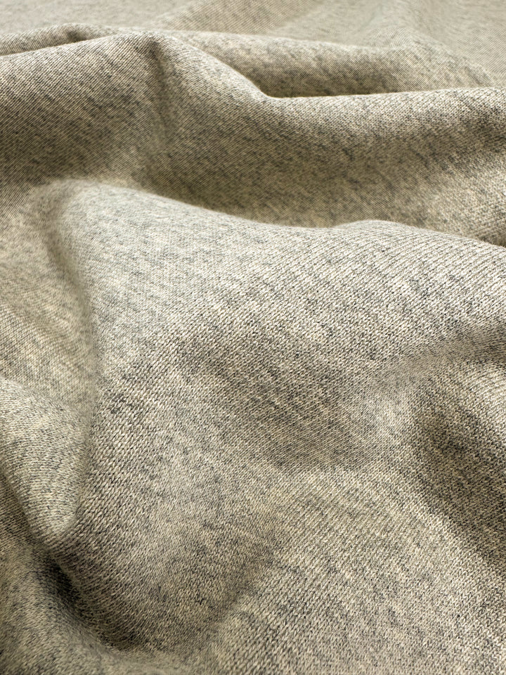 A close-up image of a piece of light grey, ultra-soft Unbrushed Fleece - Ancient Scroll - 163cm fabric from Super Cheap Fabrics, featuring a slightly heathered texture. The unbrushed fleece is draped in gentle, smooth folds, highlighting its suppleness and fine weave.