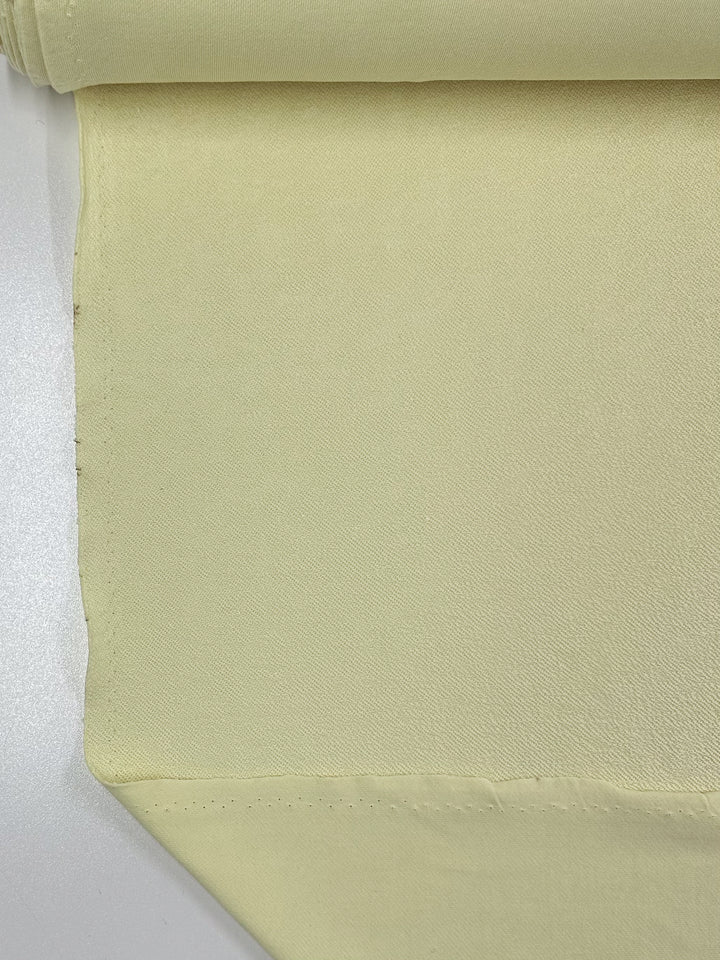 Close-up of the French Vanilla Unbrushed Fleece from Super Cheap Fabrics, showcasing its high-quality cotton fabric with a smooth, soft texture. The fabric, which measures 160cm wide, is rolled at the top, displaying a neat edge with minimal visible stitching. It is laid out flat on a white surface.