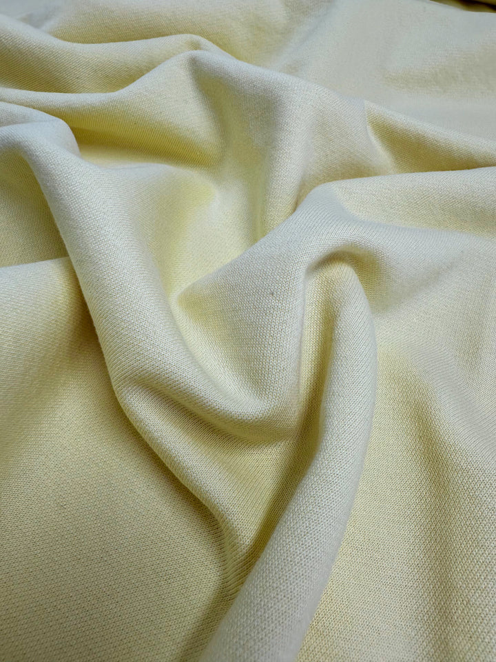 A close-up of a crumpled piece of the Super Cheap Fabrics’ Unbrushed Fleece in French Vanilla - 160cm, showcasing its texture and weave. The fabric appears soft and smooth with gentle folds and shadows, highlighting its tactile quality.