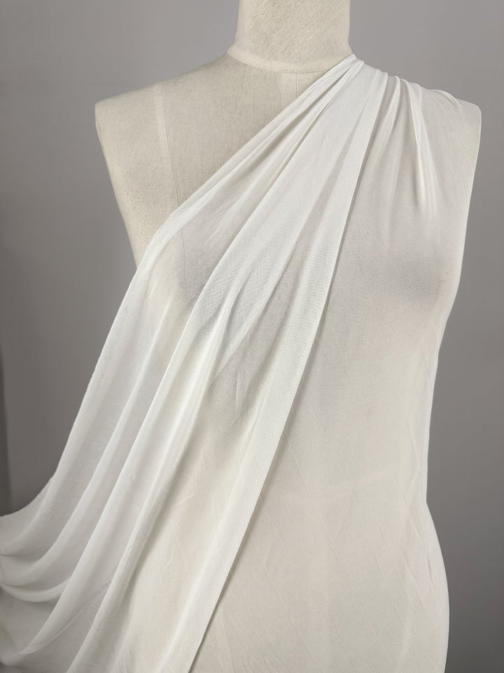 The tailor's mannequin is elegantly draped with Super Cheap Fabrics' Plain Mesh - Ivory - 145cm, a lightweight polyester fabric that hangs smoothly, highlighting its soft texture and delicate folds against the neutral background.