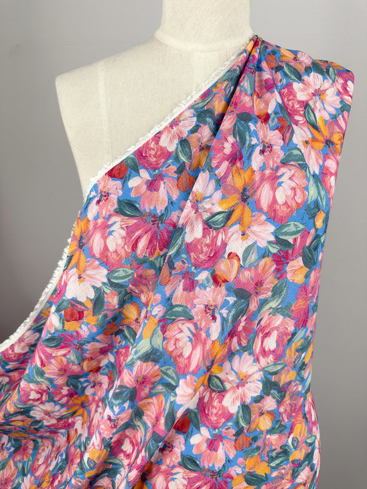 A close-up image of Super Cheap Fabrics' Soft Cotton - Acrylic - 140cm, draped over a dress form, showcases a vibrant floral-patterned fabric. The soft cotton material features colorful flowers in shades of pink, red, yellow, and green against a muted background, highlighting the intricate details in the floral design—ideal for summer fabric projects.