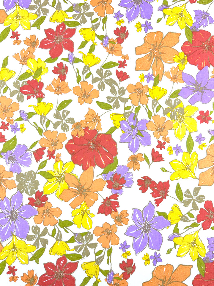 The Soft Cotton - Illustrator from Super Cheap Fabrics features a vibrant floral pattern with an array of multicolored flowers, including red, orange, yellow, and purple blossoms with green leaves on a white background. The different sizes and shapes of the flowers create a lively and colorful design that is perfect for summer fabric. This cotton material measures 140cm in width.